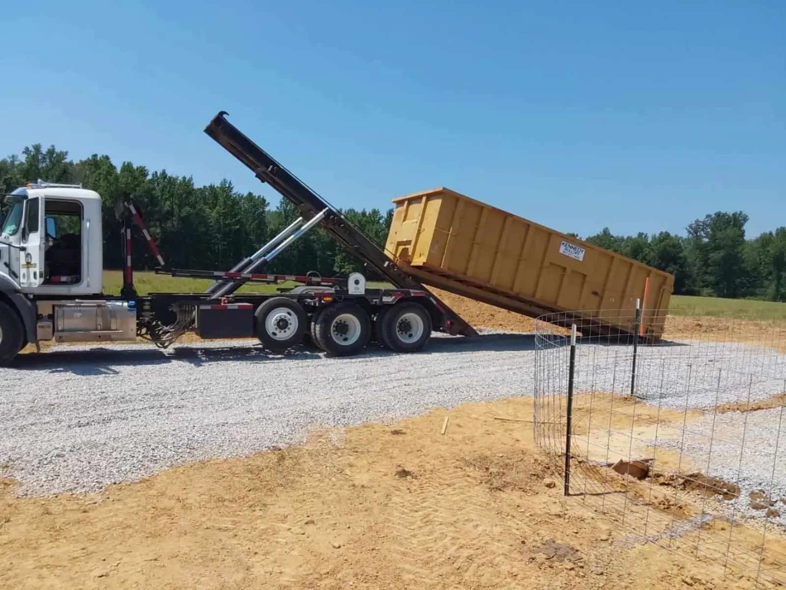 Kennedy Roll-Offs truck rolling a gold dumpster onto a graded construction pad