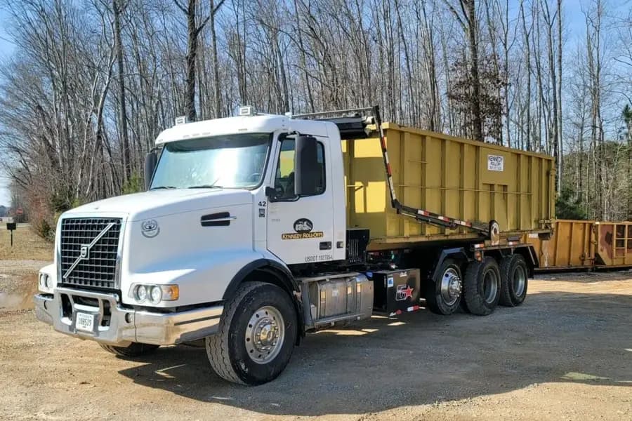 Front view of a Kennedy Roll-Offs truck hauling a yellow roll-off box