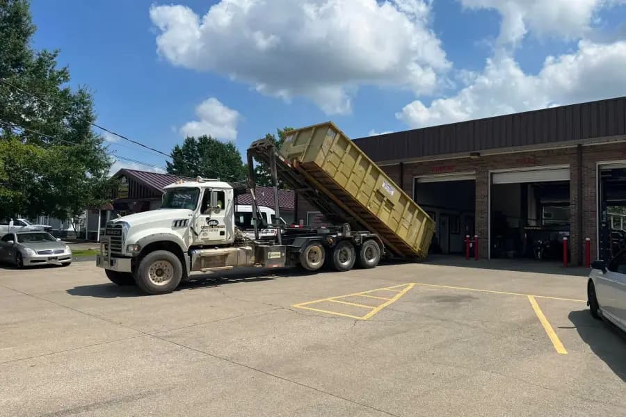 Kennedy Roll-Offs truck tilting a yellow roll-off box off its hoist in a parking lot
