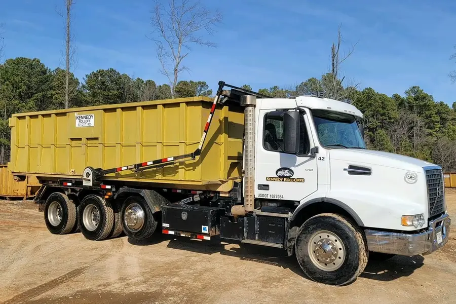 Kennedy Roll-Offs truck loaded with a yellow roll-off box in a gravel yard